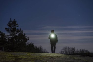 Geceleri ileri el feneri ile parlayan ormandaki açık duran adam