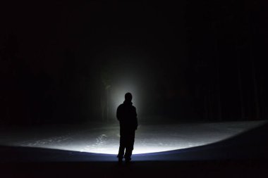 Man standing outdoors at night in tree alley shining with flashlight. Beautiful dark snowy winter night. clipart