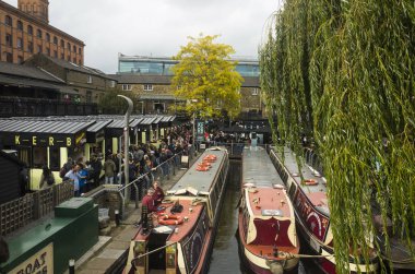 Tour boats moored on Regent's Canal inside Camden Market, London, UK, people walking around