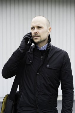 Smartphone açık havada üzerinde konuşurken siyah giysili adam portresi 