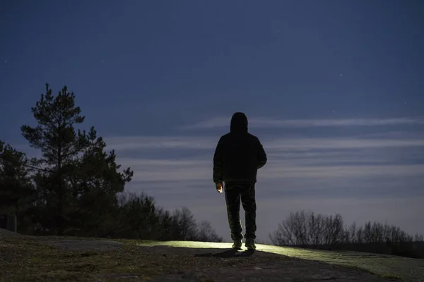 男子站在户外在夜间森林闪耀着手电筒 — 图库照片