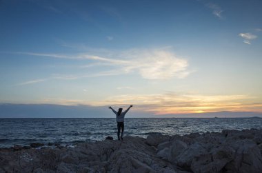 Genç bir kadın gün batımında sahilde duruyor.