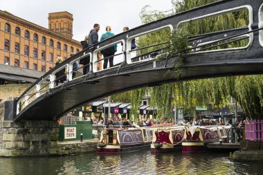 Tour boats moored on Regent's Canal inside Camden Market, London, UK, people walking around