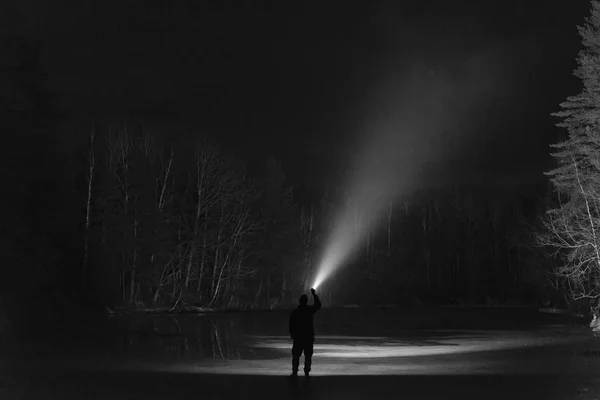 Man standing outdoor at night in forest shining forward with flashlight. Nice strong light beam. Beautiful abstract photo. Calm, peaceful and mystical image.