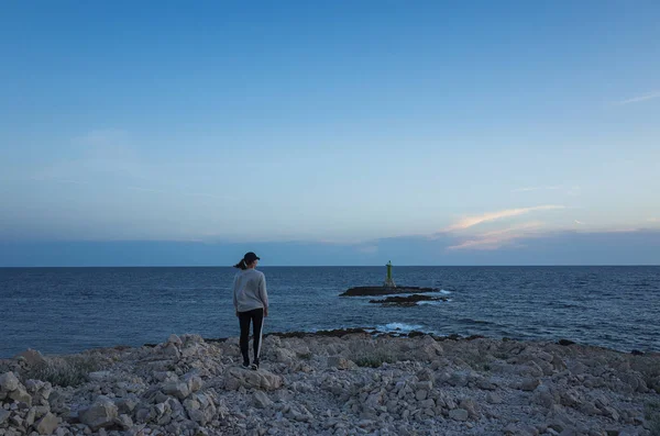 Genç bir kadın gün batımında sahilde duruyor.