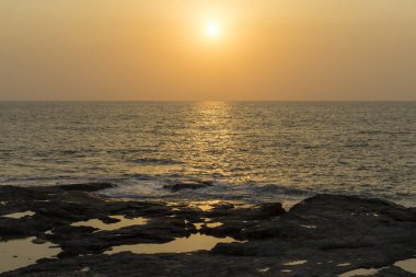 günbatımı arka planda kayalar ile kumlu plaj görünümü 