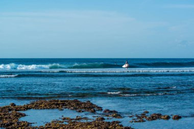 Endonezya 'daki Uluwatu Sahili yakınlarında okyanusta sörf yapan bir adamın uzaktan görünüşü