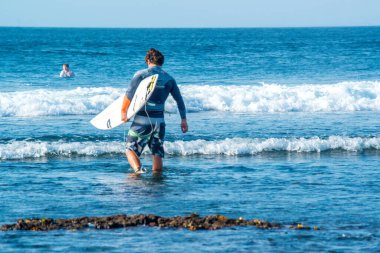Endonezya 'daki Uluwatu Sahili yakınlarında okyanusta sörf yapan bir adamın uzaktan görünüşü