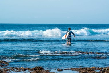Endonezya 'daki Uluwatu Sahili yakınlarında okyanusta sörf yapan bir adamın uzaktan görünüşü