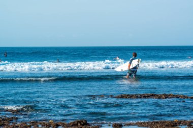 Endonezya 'daki Uluwatu Sahili yakınlarında okyanusta sörf yapan bir adamın uzaktan görünüşü