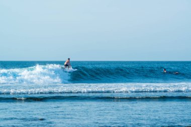Endonezya 'daki Uluwatu Sahili yakınlarında okyanusta sörf yapan bir adamın uzaktan görünüşü