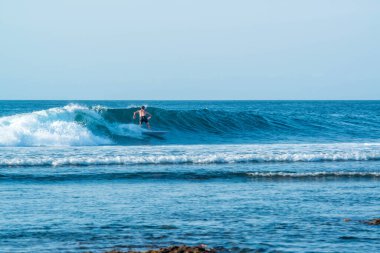 Endonezya 'daki Uluwatu Sahili yakınlarında okyanusta sörf yapan bir adamın uzaktan görünüşü