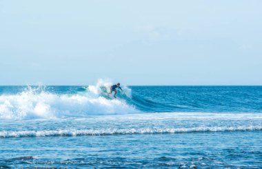 Endonezya 'daki Uluwatu Sahili yakınlarında okyanusta sörf yapan bir adamın uzaktan görünüşü