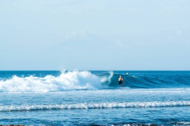 Endonezya 'daki Uluwatu Sahili yakınlarında okyanusta sörf yapan bir adamın uzaktan görünüşü