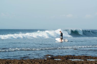 Endonezya 'daki Uluwatu Sahili yakınlarında okyanusta sörf yapan bir adamın uzaktan görünüşü