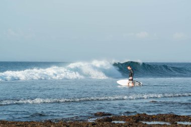 Endonezya 'daki Uluwatu Sahili yakınlarında okyanusta sörf yapan bir adamın uzaktan görünüşü