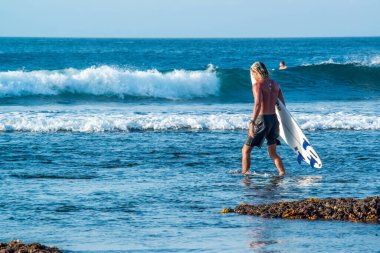 Endonezya 'daki Uluwatu Sahili yakınlarında okyanusta sörf yapan bir adamın uzaktan görünüşü