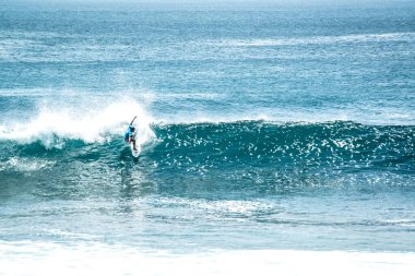Endonezya 'daki Uluwatu Sahili yakınlarında okyanusta sörf yapan bir adamın uzaktan görünüşü