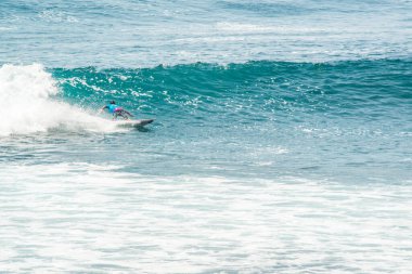 Endonezya 'daki Uluwatu Sahili yakınlarında okyanusta sörf yapan bir adamın uzaktan görünüşü