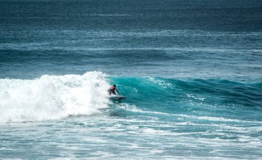 Endonezya 'daki Uluwatu Sahili yakınlarında okyanusta sörf yapan bir adamın uzaktan görünüşü