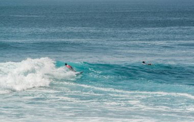 Endonezya 'daki Uluwatu Sahili yakınlarında okyanusta sörf yapan bir adamın uzaktan görünüşü