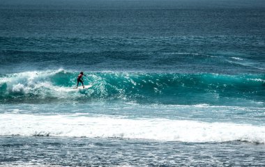 Endonezya 'daki Uluwatu Sahili yakınlarında okyanusta sörf yapan bir adamın uzaktan görünüşü