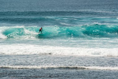 Endonezya 'daki Uluwatu Sahili yakınlarında okyanusta sörf yapan bir adamın uzaktan görünüşü