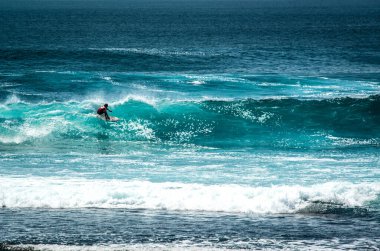 Endonezya 'daki Uluwatu Sahili yakınlarında okyanusta sörf yapan bir adamın uzaktan görünüşü