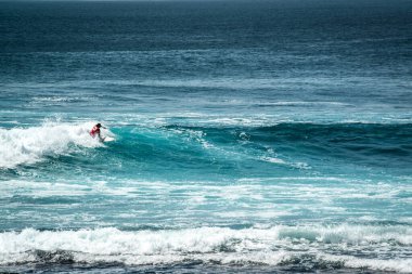 Endonezya 'daki Uluwatu Sahili yakınlarında okyanusta sörf yapan bir adamın uzaktan görünüşü