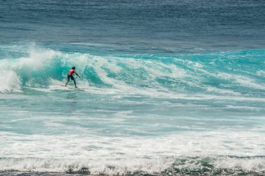 Endonezya 'daki Uluwatu Sahili yakınlarında okyanusta sörf yapan bir adamın uzaktan görünüşü