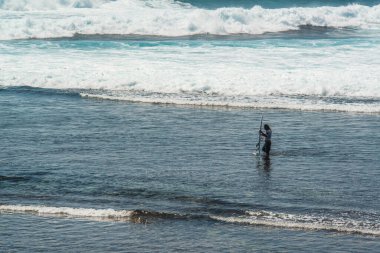 Endonezya 'daki Uluwatu Sahili yakınlarında okyanusta sörf yapan bir adamın uzaktan görünüşü