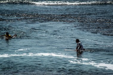 Endonezya 'daki Uluwatu Sahili yakınlarında okyanusta sörf yapan bir adamın uzaktan görünüşü
