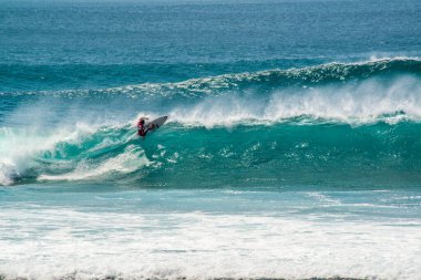 Endonezya 'daki Uluwatu Sahili yakınlarında okyanusta sörf yapan bir adamın uzaktan görünüşü