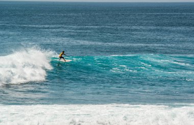 Endonezya 'nın Uluwatu Sahili yakınlarında okyanusta sörf yapan bir adam.