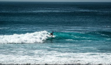 Endonezya 'nın Uluwatu Sahili yakınlarında okyanusta sörf yapan bir adam.