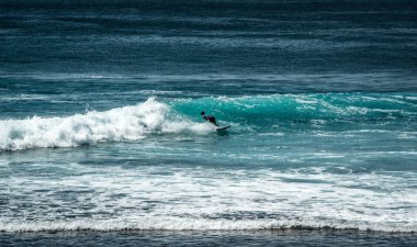 Endonezya 'nın Uluwatu Sahili yakınlarında okyanusta sörf yapan bir adam.