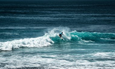 Endonezya 'nın Uluwatu Sahili yakınlarında okyanusta sörf yapan bir adam.