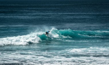 Endonezya 'nın Uluwatu Sahili yakınlarında okyanusta sörf yapan bir adam.