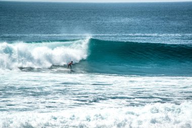 Endonezya 'nın Uluwatu Sahili yakınlarında okyanusta sörf yapan bir adam.