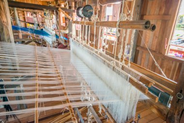 İnsanlar atölyede el dokuma tezgahıyla çalışıyorlar..