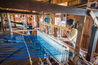 İnsanlar atölyede el dokuma tezgahıyla çalışıyorlar..