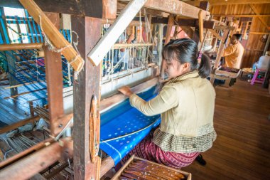İnsanlar atölyede el dokuma tezgahıyla çalışıyorlar..