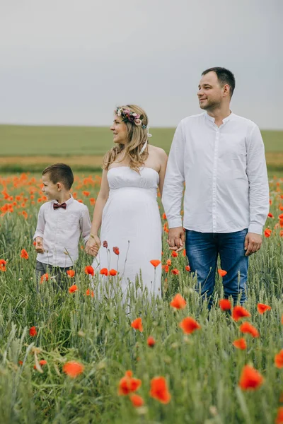 Familia caminando en el campo de amapola tomados de la mano sonriendo — Foto de Stock