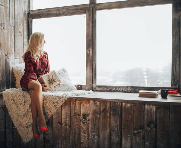 Schöne blonde Frau hält eine Geschenkschachtel in der Hand und schaut aus dem Fenster — Stockfoto