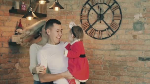Щаслива сім'я з маленькою дочкою в костюмі санта на фоні різдвяних вогнів — стокове відео