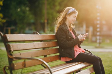 Kamu parkında cep telefonunda gezinen bir kadın. Şehir, şehir geçmişi. Parktaki mutlu kız cep telefonu kullanıyor..