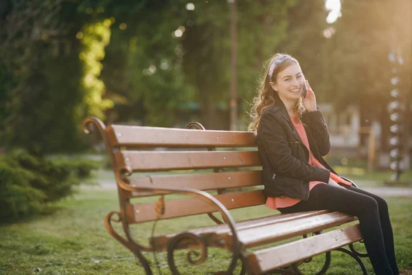 Jovem mulher vestida de elegante desgaste ter conversa telefônica com o namorado. Discussão de ideias para fins de semana durante a pausa de trabalho sentado ao ar livre no banco da cidade . — Fotografia de Stock