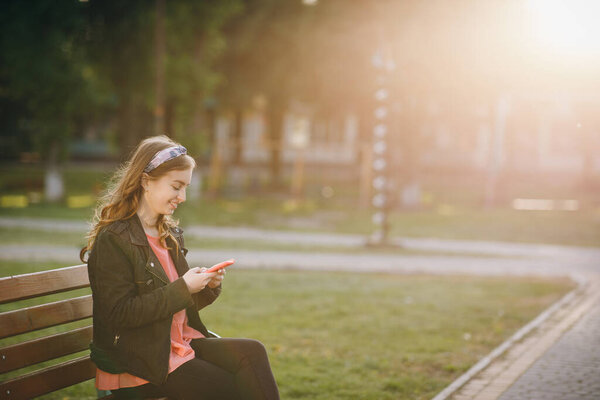 Девушка смеется и читает что-то на своем смартфоне. Веселая молодая женщина, общающаяся по смартфону во время прогулки в парке
.