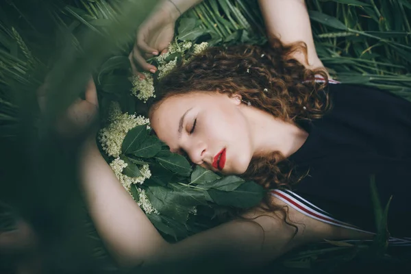 Uma menina bonita nova no vestido preto deitado em uma grama e sonhando — Fotografia de Stock
