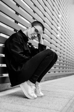 Bir duvara oturan kısa saçlı bir kadın